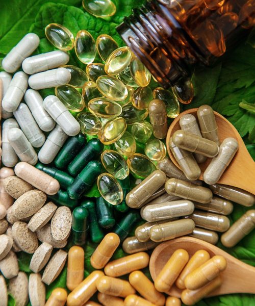 Capsules herb supplements on green leaves background. Selective focus.